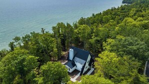 A house surrounded by dense forest with a view of the sea. - Luxe Lakefront Home · Sleeps 10 · Jacksonport (Sturgeon Bay)