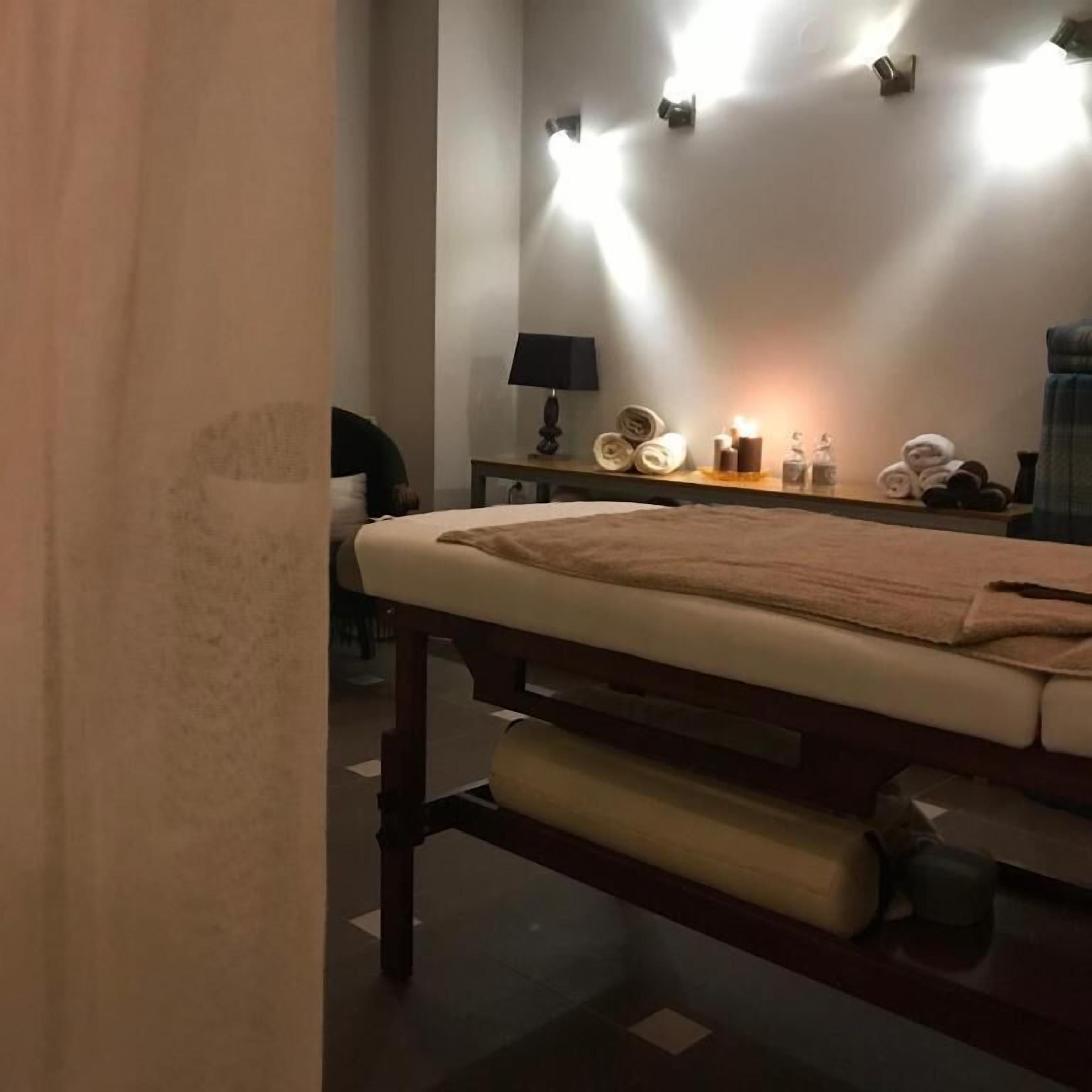 A massage table with a towel, a lamp, and rolled towels on a shelf.