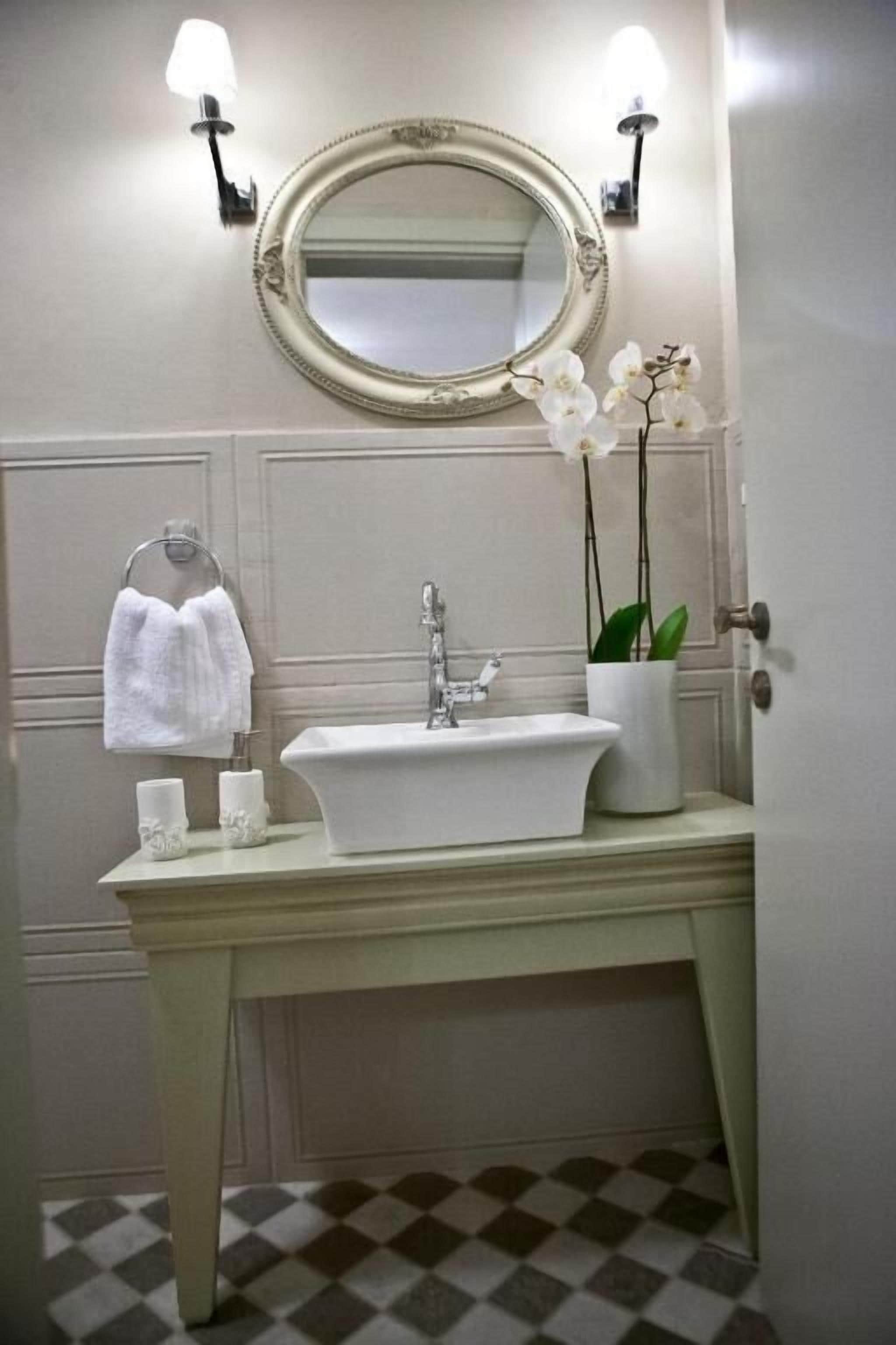 A bathroom with a white sink, a mirror with an ornate frame, and a potted orchid.