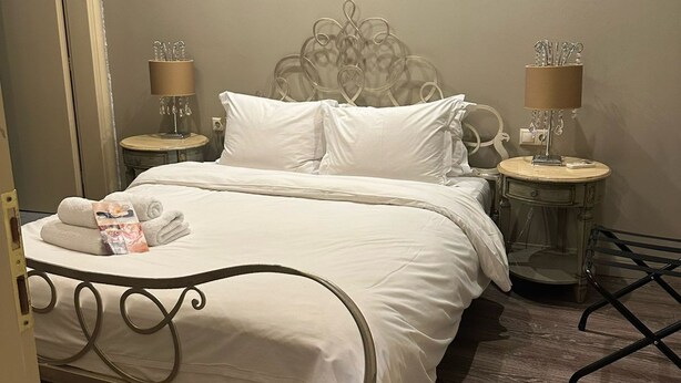 Una cama bien hecha con sábanas blancas, dos mesitas de noche con lámparas y un suelo de madera.