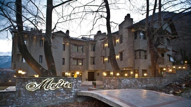 Un edificio de varios pisos de piedra con un puente de piedra en primer plano, rodeado de árboles.
