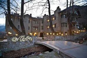 A multi-story stone building with a stone bridge in front, surrounded by trees. - Melies Boutique Hotel (Almopia)