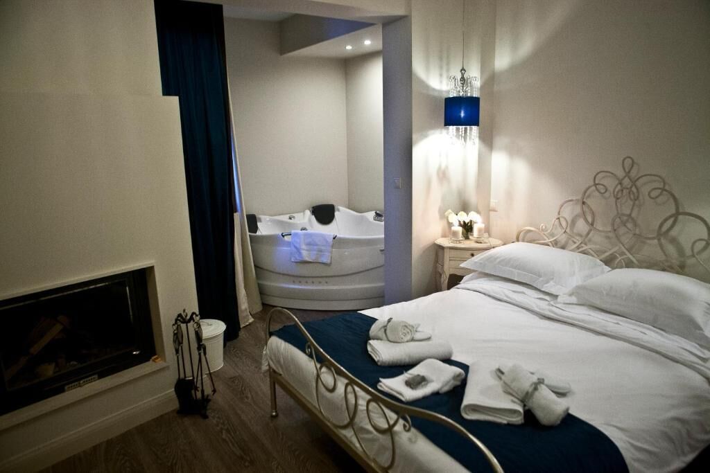 Ett hotellrum med en säng, ett badkar, en öppen spis och ett nattduksbord med en lampa.