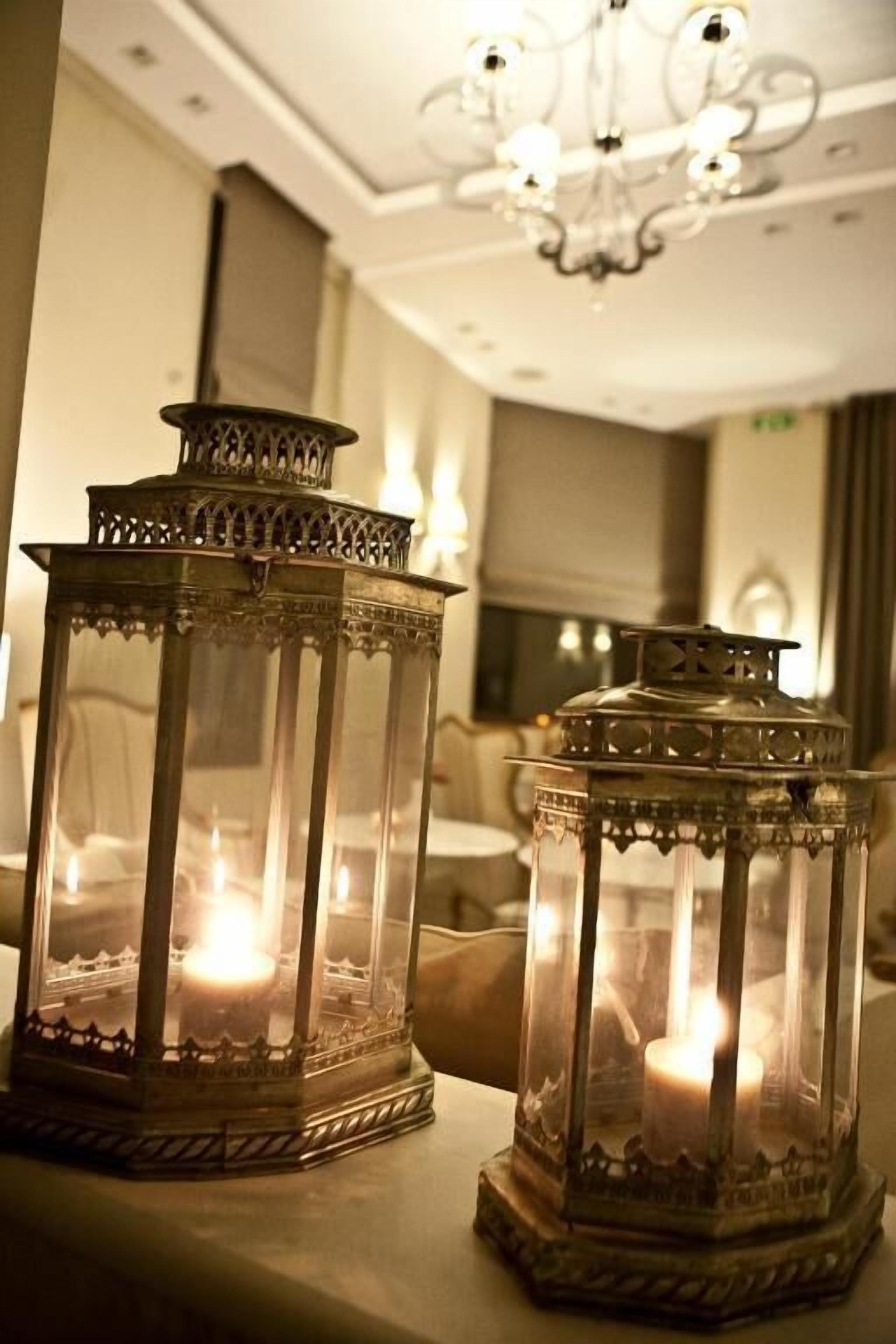 Dos faroles ornamentales con velas en su interior, colocados sobre una mesa en una habitación con una araña.