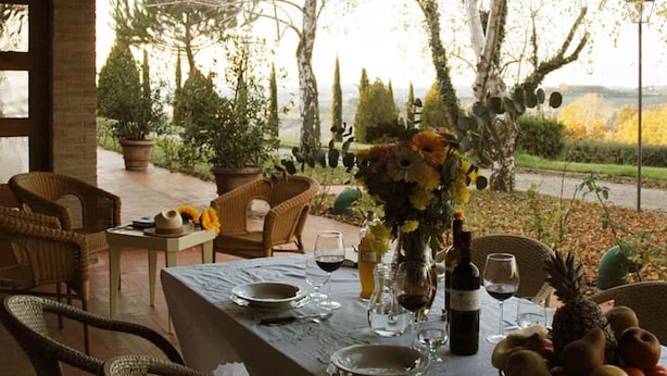 An outdoor dining area with wicker chairs, a table set for two with wine glasses, a bottle of wine, and a fruit bowl. - Villa Panconesi (Montespertoli)