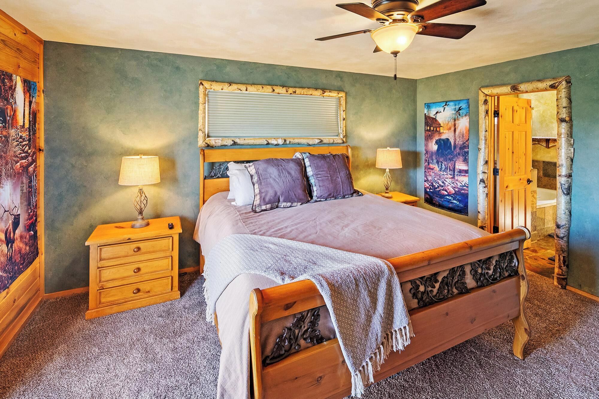A bedroom with a wooden bed, two bedside tables with lamps, a ceiling fan, and a large mirror.