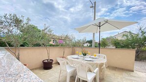 An outdoor patio with a table set for two, surrounded by potted plants and a large umbrella. - Apartment in Silo/insel Krk 13424 (Dobrinj)