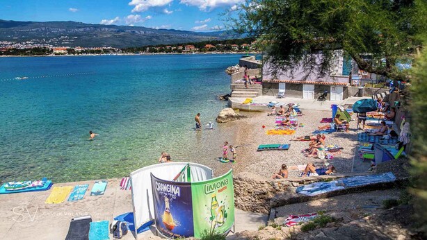 A beach with clear water, people sunbathing, and a view of a distant town. - Apartment in Silo/insel Krk 13424 (Dobrinj)