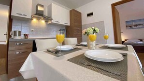 A modern kitchen with white cabinets, a stainless steel range hood, and a dining area set with a table, plates, and glasses of orange juice. - Apartment in Silo/insel Krk 13424 (Dobrinj)