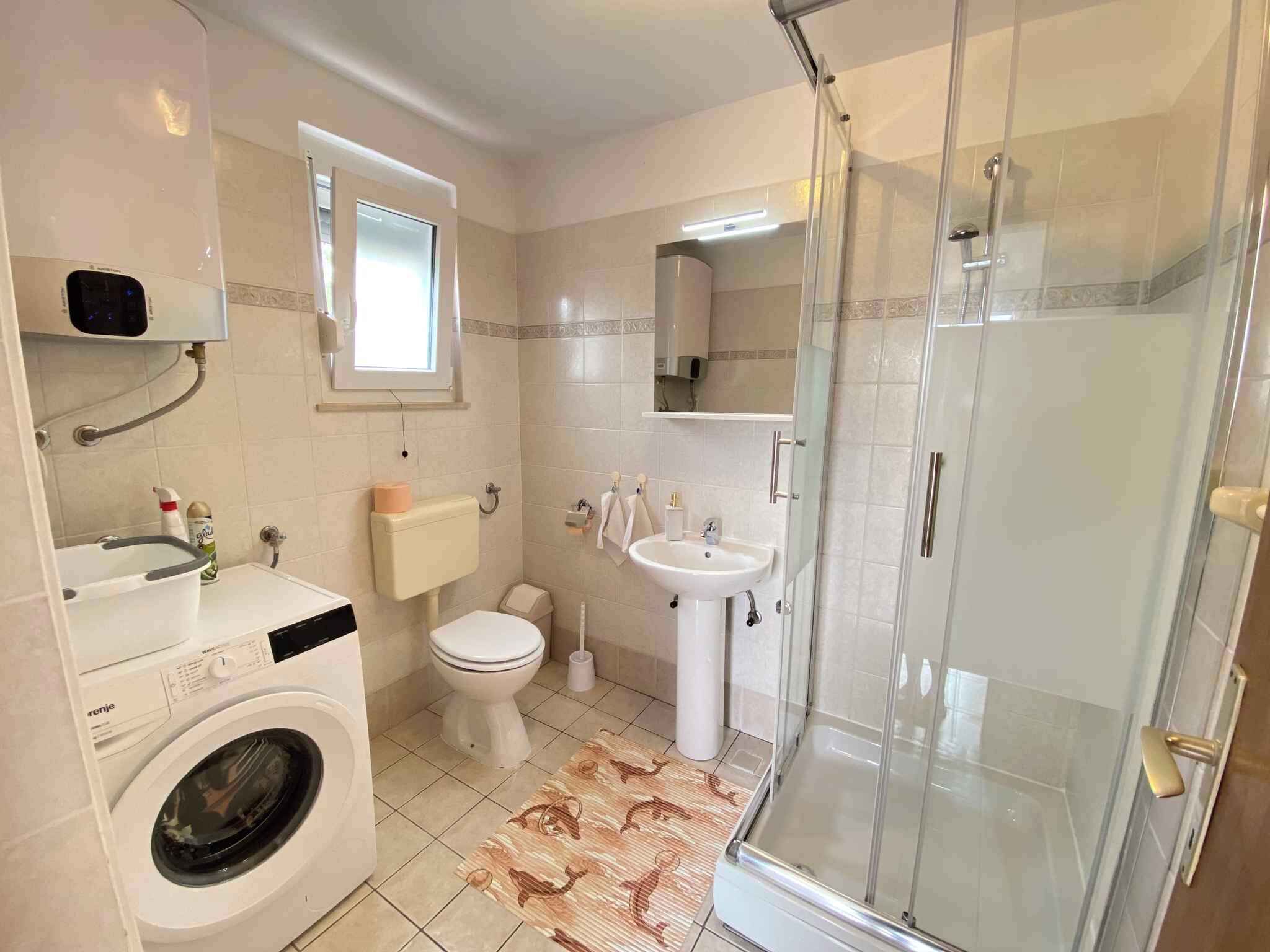 A compact bathroom with a washing machine, toilet, sink, and glass-enclosed shower.