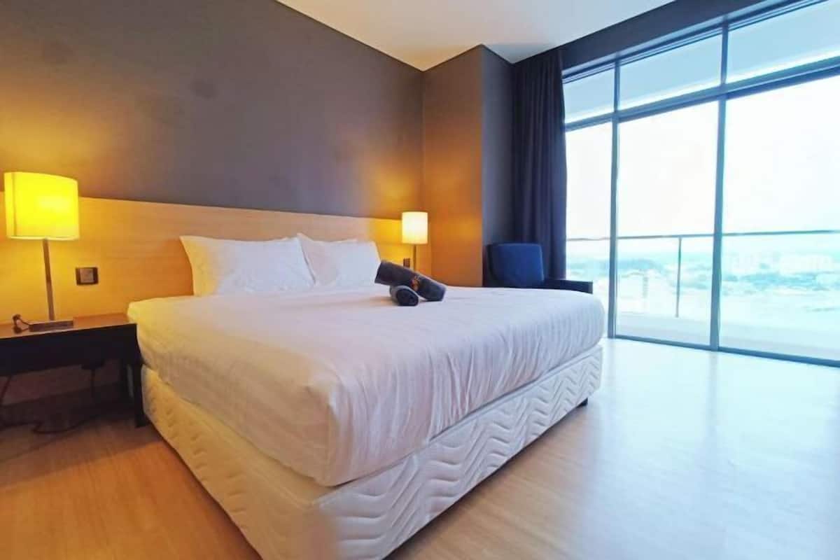 Habitación de hotel con una cama grande, dos lámparas de noche, una silla y un ventanal con vistas.