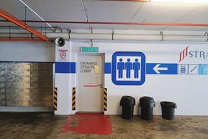 Een inkom naar een hal met een richtingsbord, een deur met de tekst 'Entrance Straits Lobby' en een prullenbak.