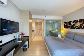 A modern hotel room with a flat-screen TV, a sofa, a bedside table with a lamp, and a glass shower enclosure. - Straits Residence Melaka Private Suites (Melaka)