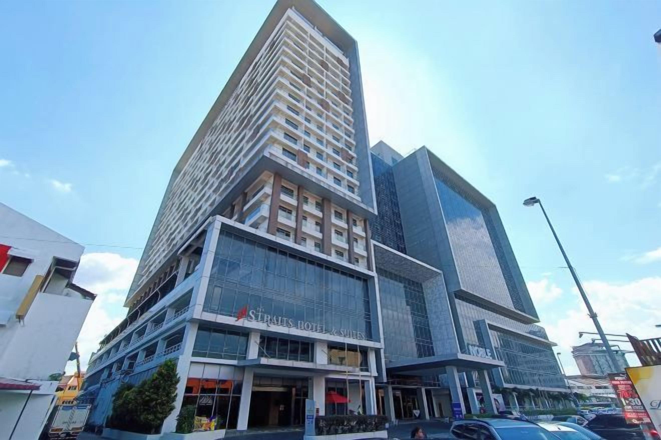 Un hotel de varios pisos con fachada de vidrio moderna, ubicado en un entorno urbano con edificios cercanos.