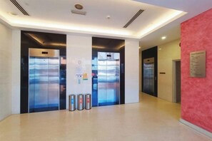 An interior corridor with two elevators, a trash bin, and a wall-mounted sign. - Straits Residence Melaka Private Suites (Melaka)