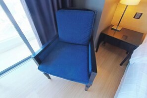 Ein Hotelzimmer mit einem blauen Sessel, einem Nachttisch mit Lampe und einem Bett mit weißer Bettwäsche.