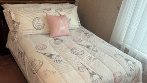 Un lit avec une couette et des oreillers à motifs parisiens, une tête de lit en bois et une fenêtre avec des stores.