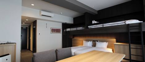 A modern hotel room with bunk beds, a wooden dining table, and a kitchenette.