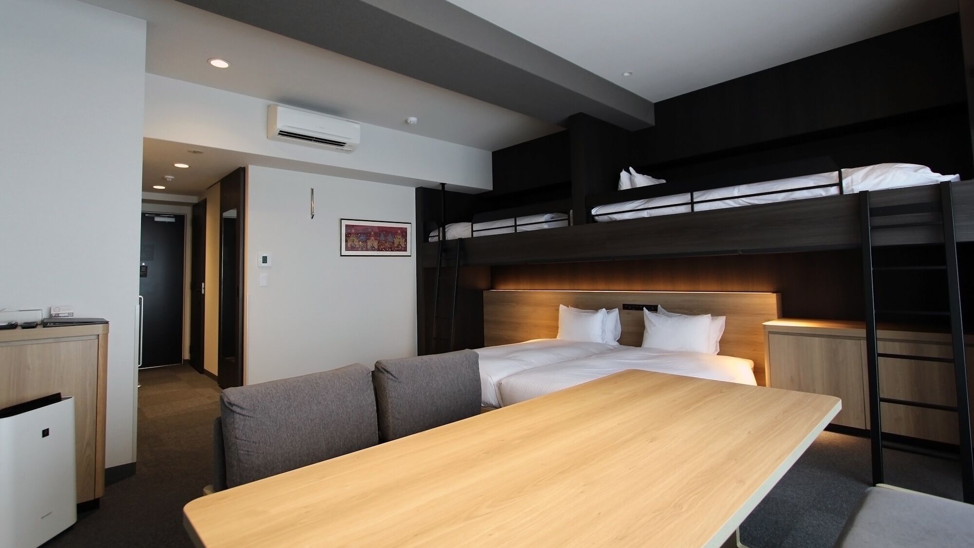 Habitación con literas, una mesa de madera, un sofá y un escritorio con una silla.