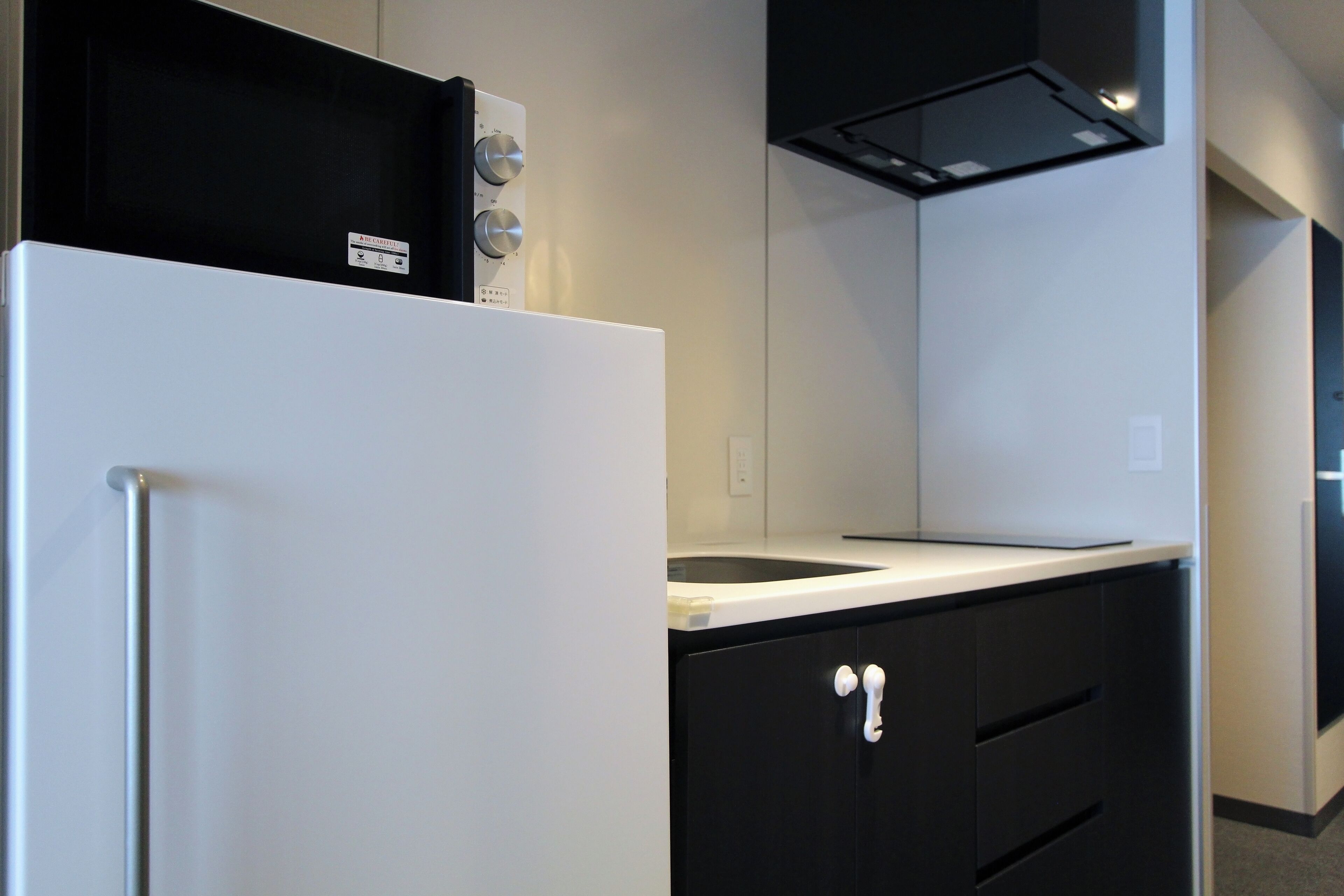 A modern kitchen with a white refrigerator, black cabinets, and a black range hood.