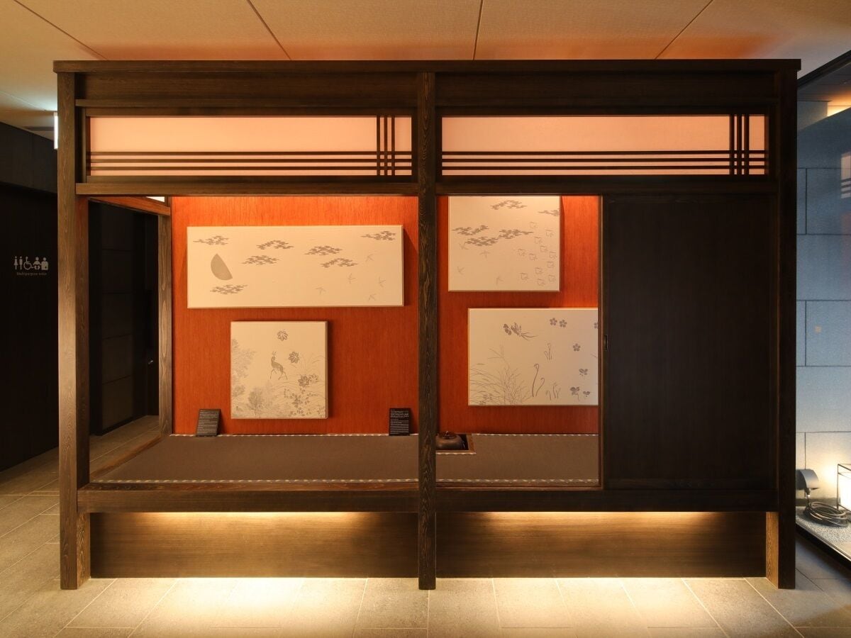 Una habitación tradicional japonesa con suelo de tatami, una mesa de madera baja y obras de arte en las paredes.
