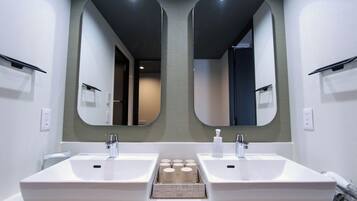Un baño moderno con dos lavamanos, un espejo y un mueble de almacenamiento con artículos de aseo.