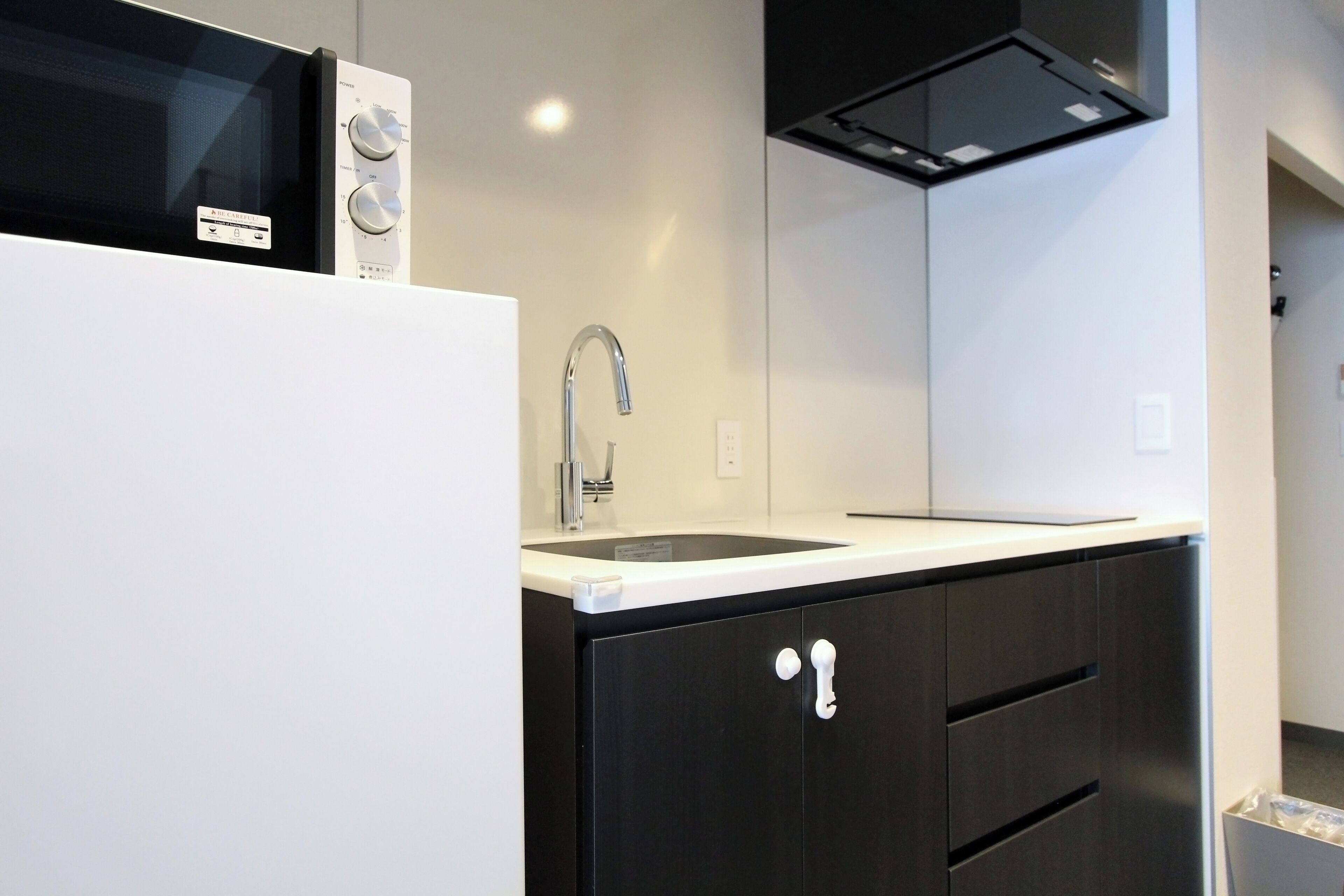 Una cocina moderna con microondas integrado, un lavamanos de acero inoxidable y muebles negros.