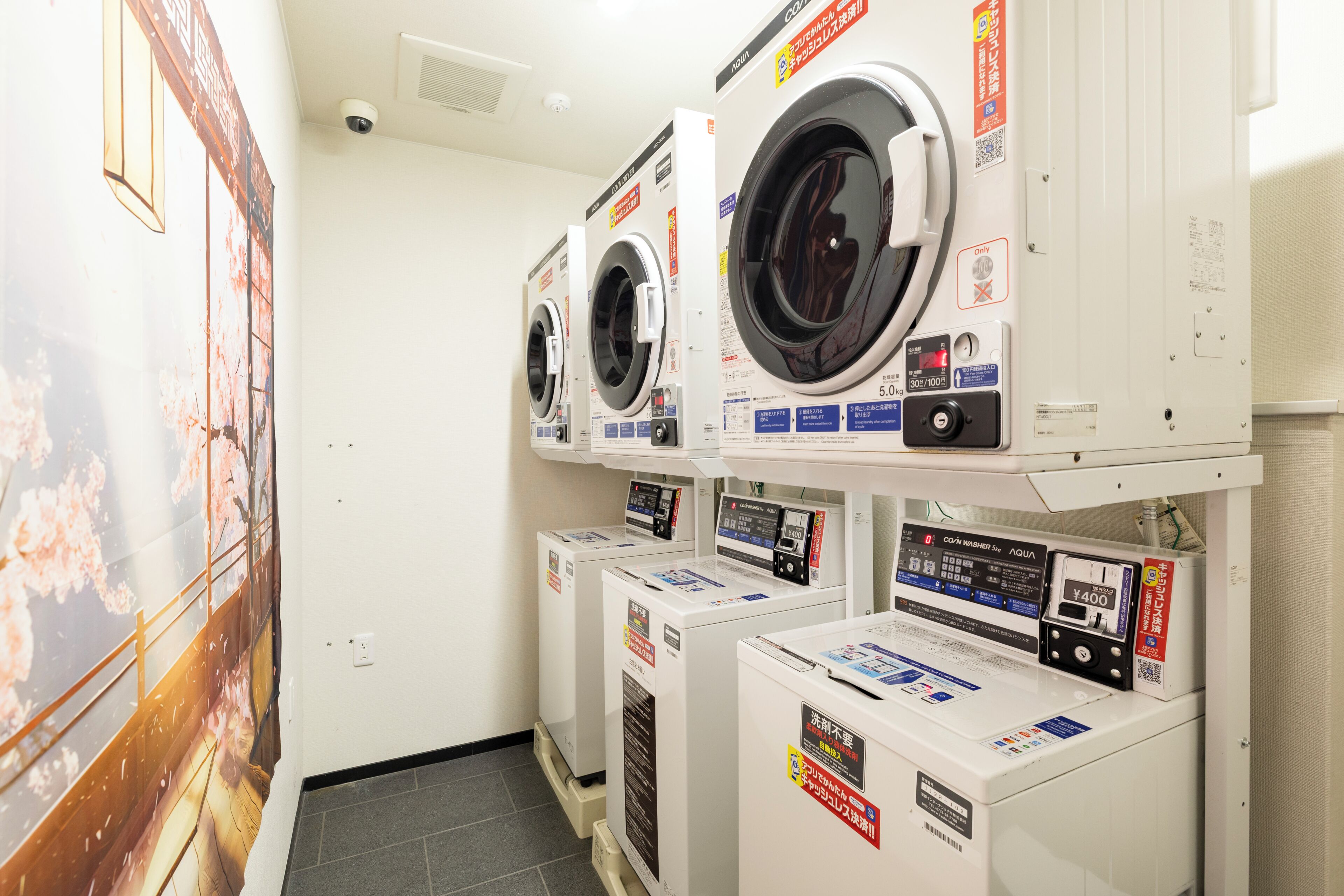 A laundry facility with multiple washing machines, a poster on the wall, and a tiled floor.