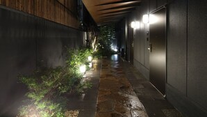 A narrow, dimly lit corridor with a stone pathway, wooden panel walls, and a metal door on the right. - KOKO HOTEL Residence Kyoto Nijo Castle (Kyoto)