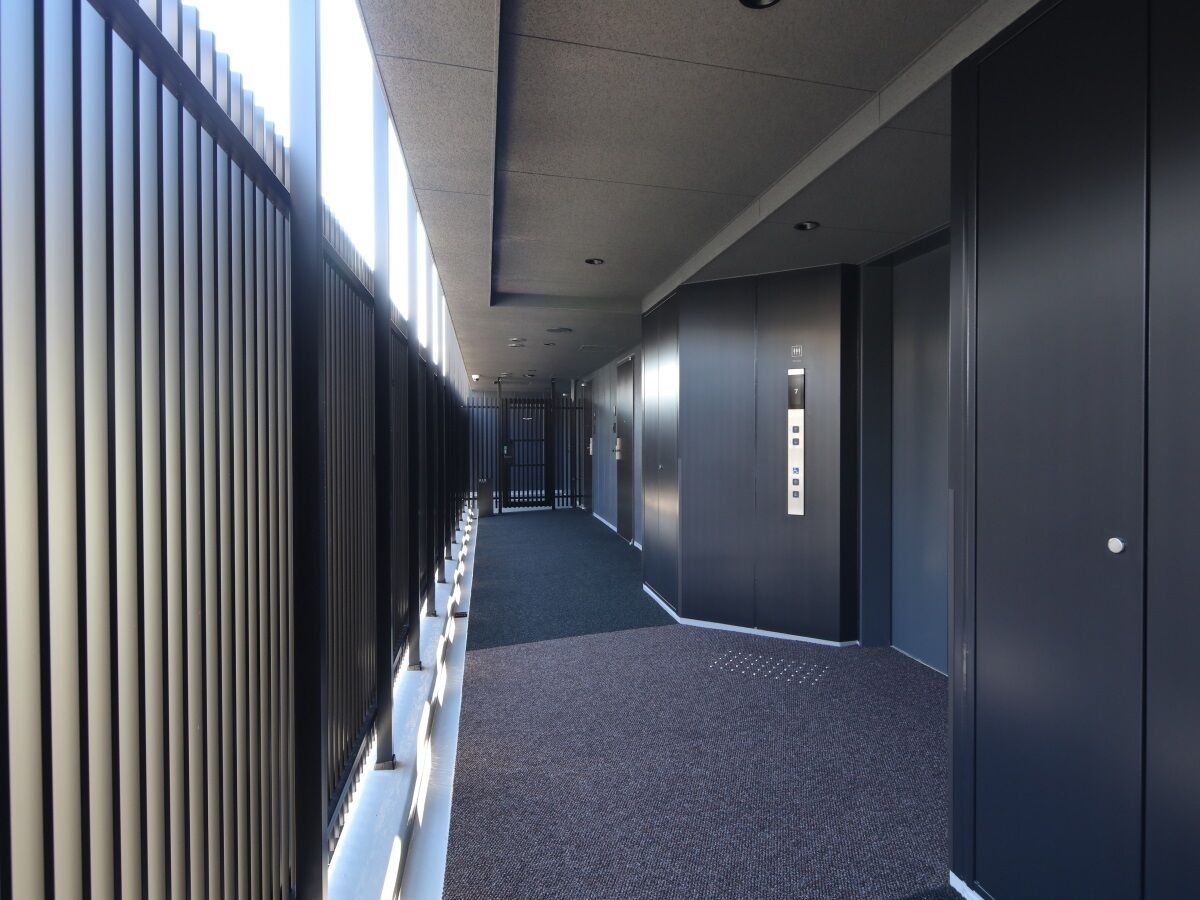 A long, narrow hallway with a patterned carpet, a metal railing on one side, and a series of doors on the other.