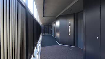 A long, narrow hallway with a patterned carpet, a metal railing on one side, and a series of doors on the other.