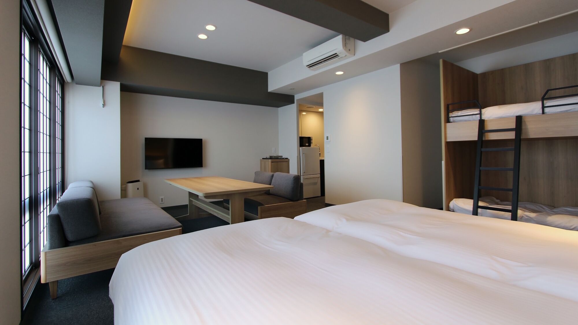 Habitación de hotel con cama, literas, escritorio, silla, televisor y aire acondicionado.