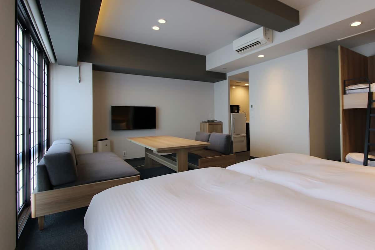 A hotel room with a bed, bunk beds, a desk, a chair, a TV, and an air conditioning unit.
