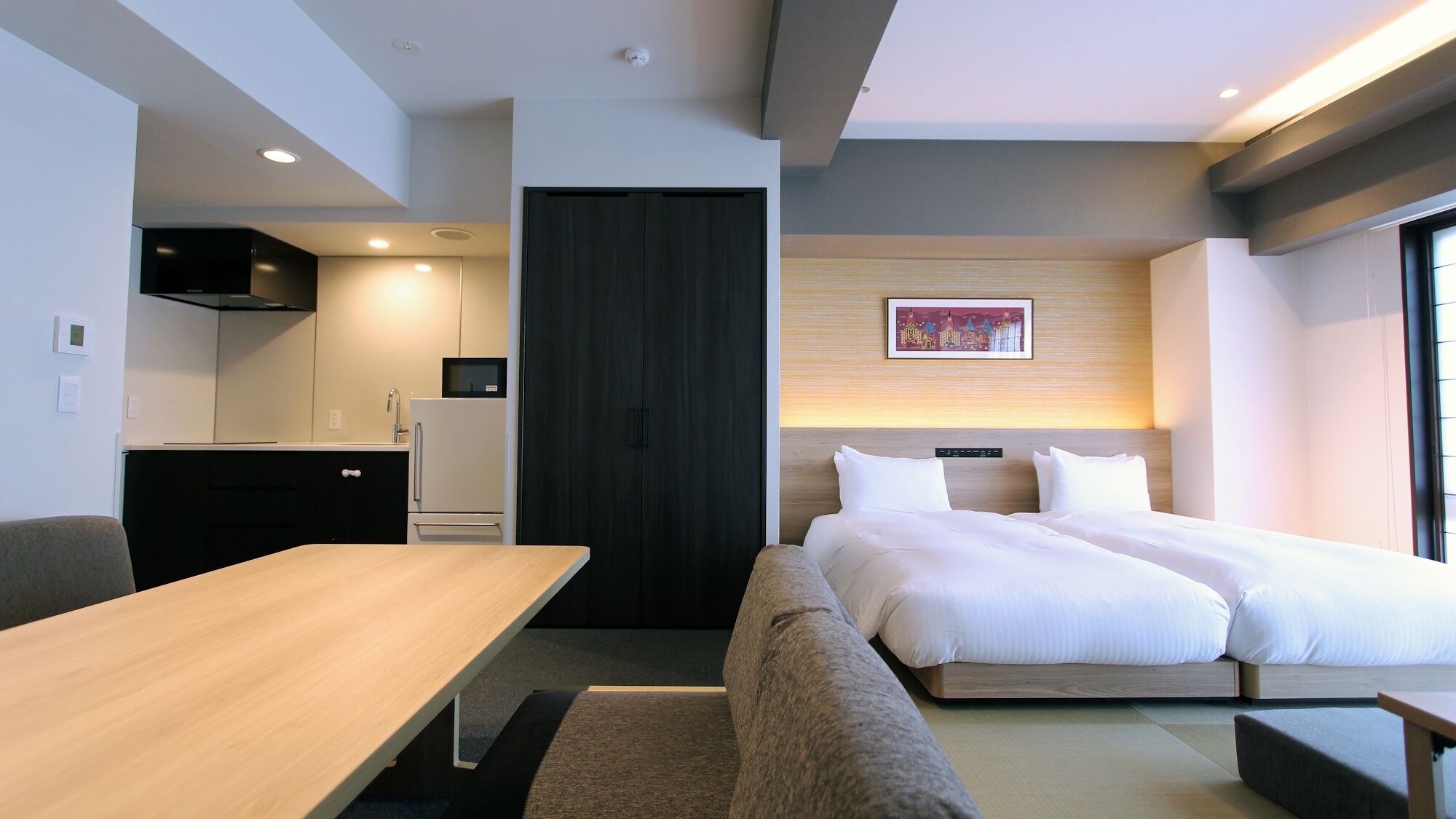 Une chambre d’hôtel moderne équipée d’un lit, d’un bureau, d’une kitchenette et offrant une vue sur la ville.
