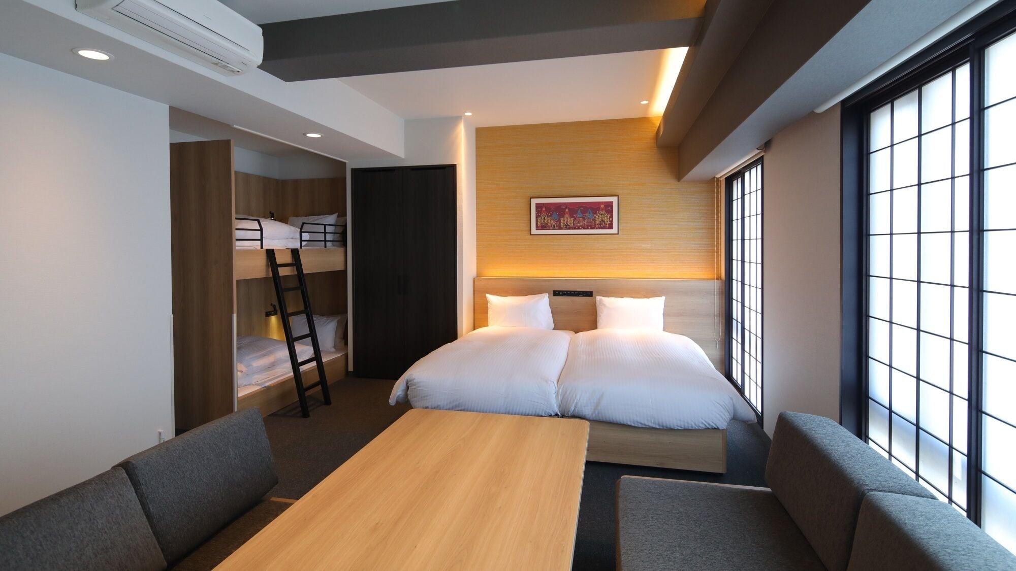Habitación de hotel con literas, una cama, un escritorio y un ventanal grande.