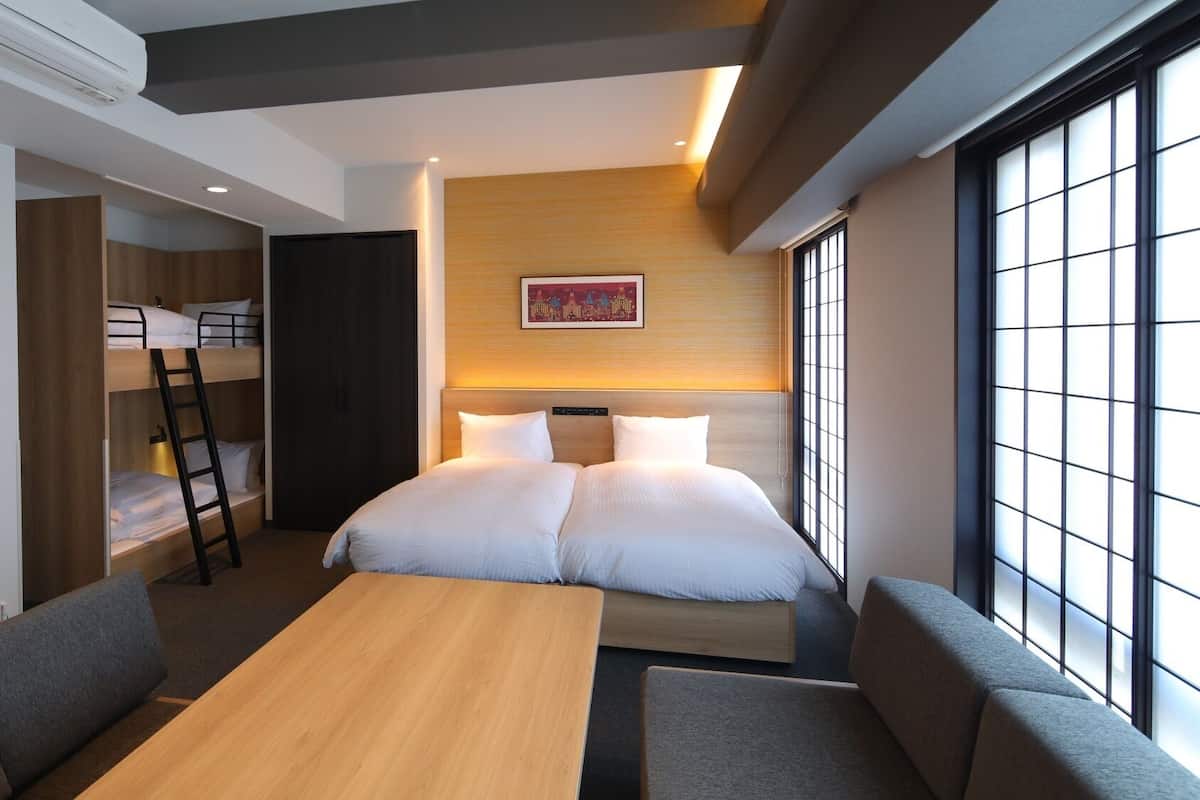 A hotel room with bunk beds, a bed, a desk, and a large window.