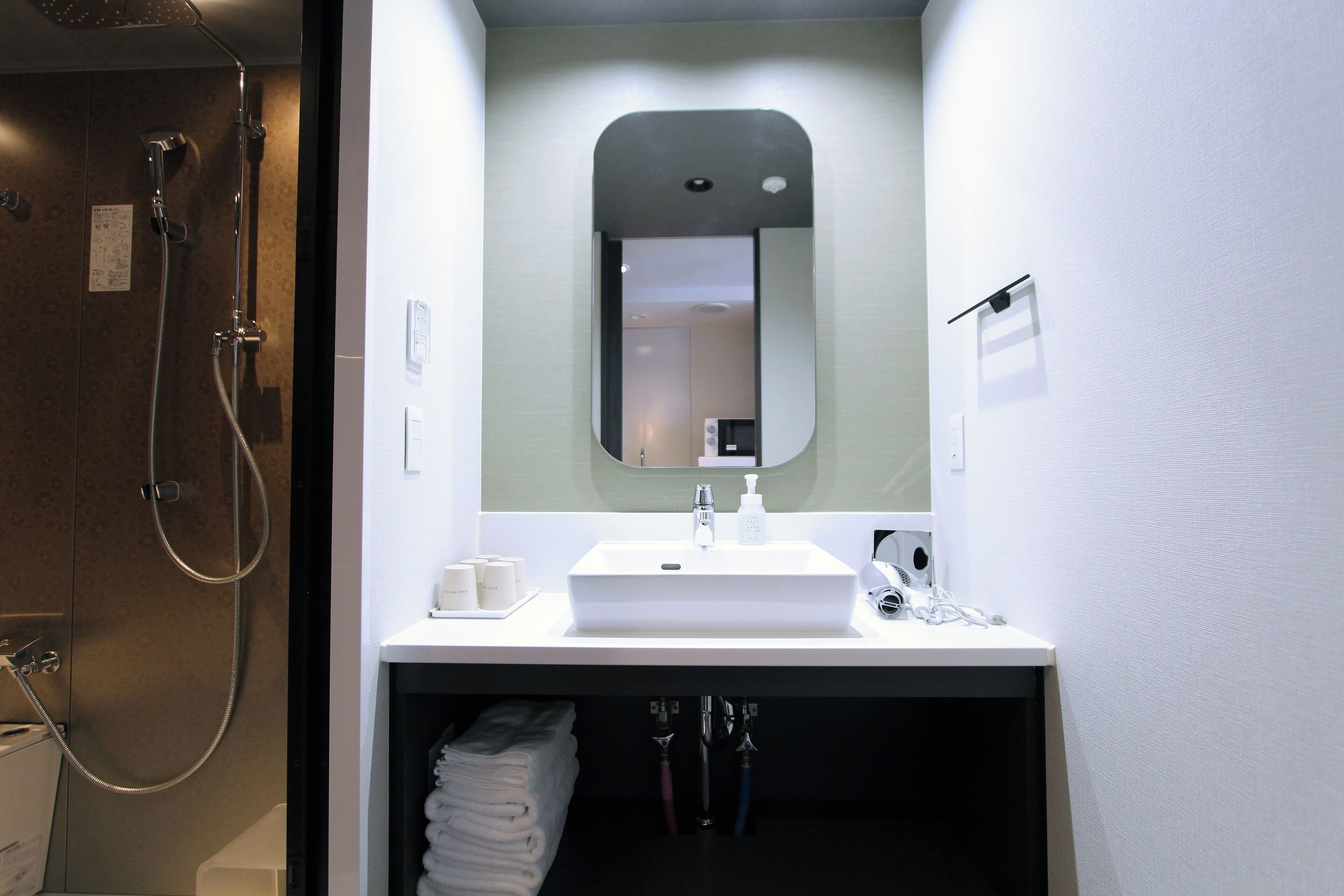 A modern bathroom with a white sink, mirror, and shower. There are towels and toiletries visible.