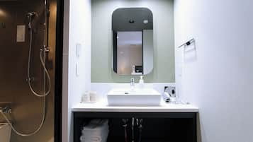 A modern bathroom with a white sink, mirror, and shower. There are towels and toiletries visible.