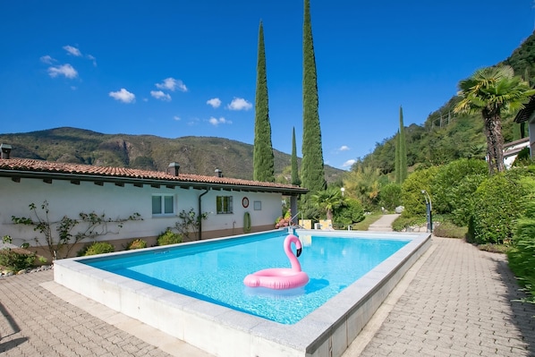 Una piscina con un flotador de flamenco rosa, rodeada de vegetación y una montaña al fondo.