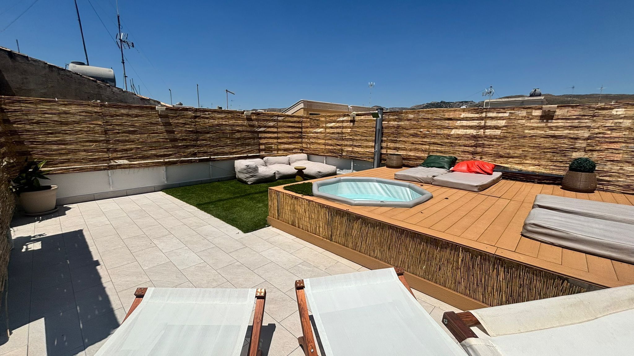 A rooftop patio with a hot tub, lounge area, and a small lawn.