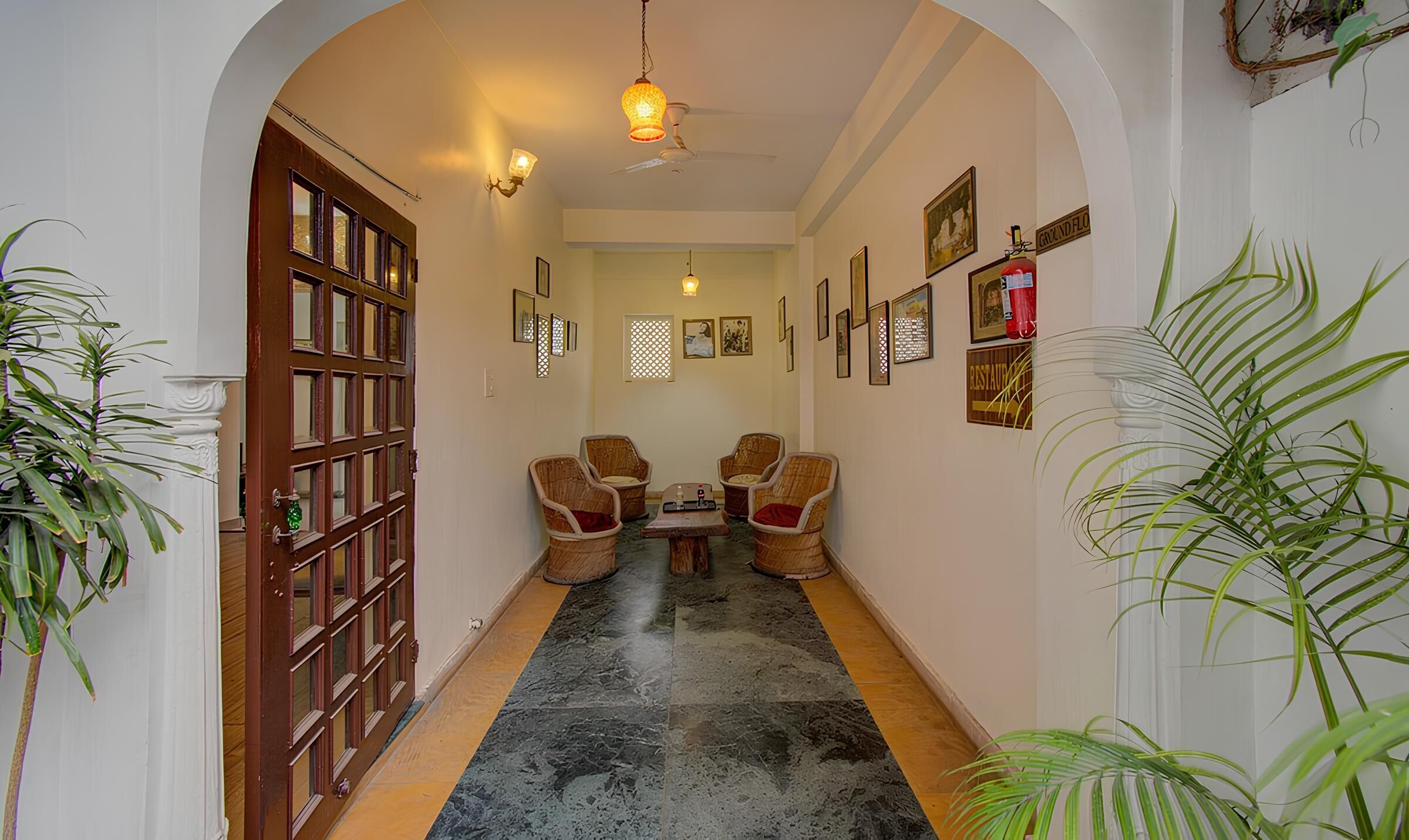 A hallway with a wooden door, two wicker chairs, a small table, and various framed pictures on the walls.