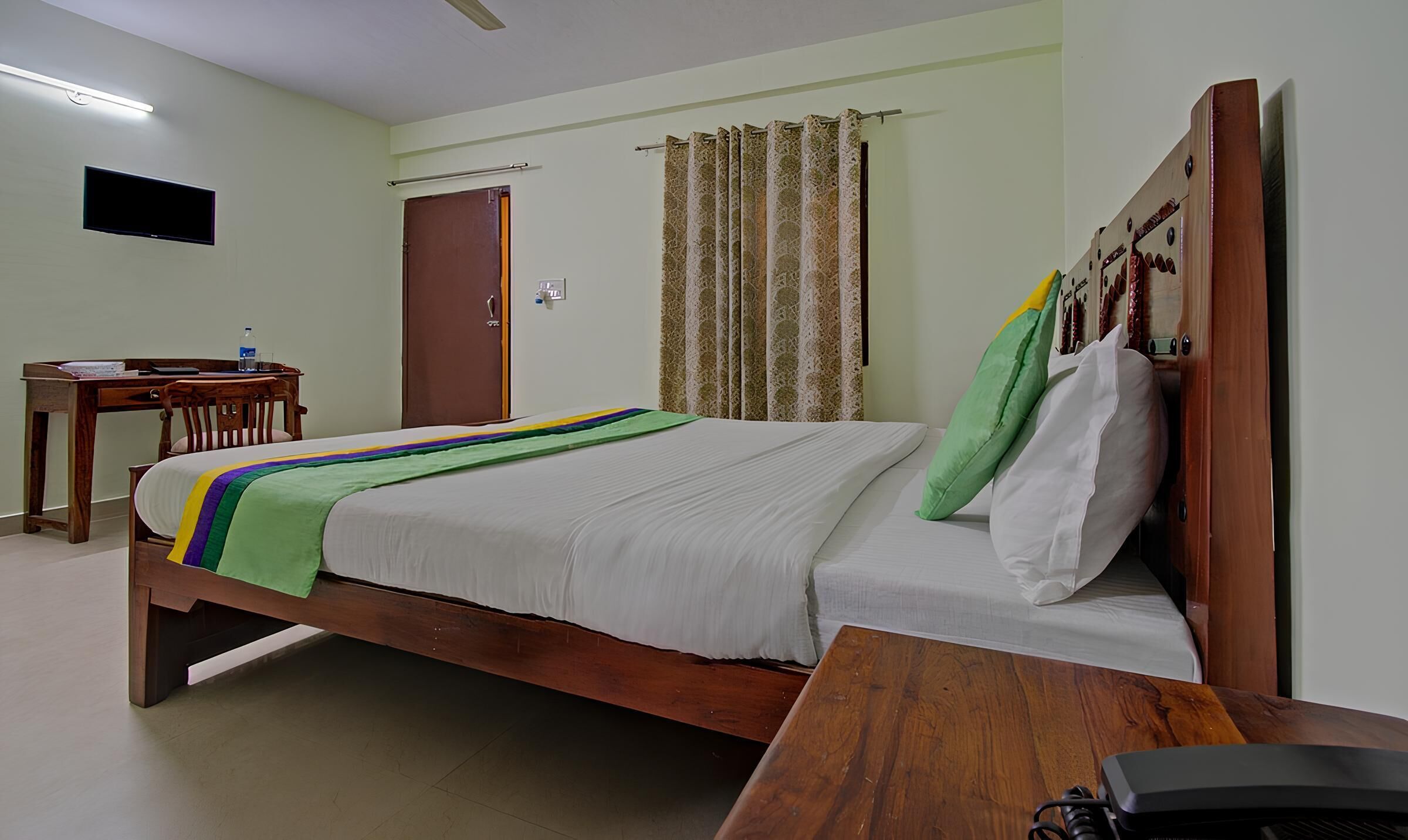 A hotel room with a bed, a desk, a chair, a television, and a curtain.