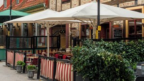 Een geplaveid straatje met terrasjes van een restaurant, omringd door historische gebouwen met rode dakpannen en bakstenen gevels.