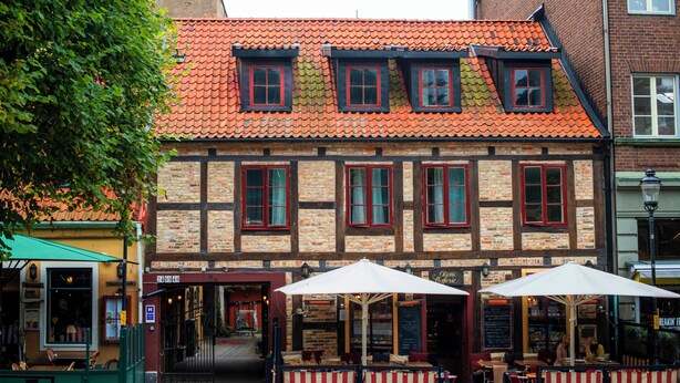Een traditioneel vakwerkhuis met een rode pannendak, terras met gestreepte luifels, en een zichtbare ingang.