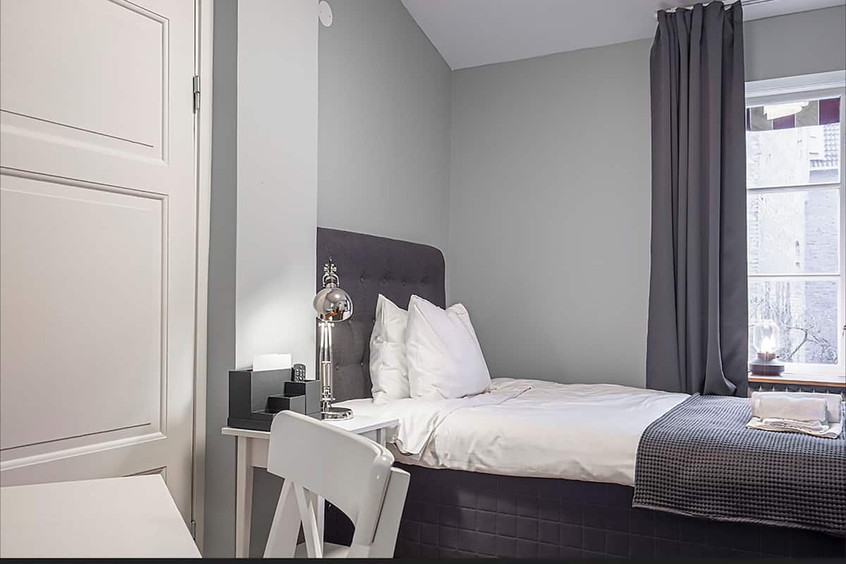 Une chambre moderne avec un lit, une table de chevet, une lampe et une vue sur la ville par la fenêtre.
