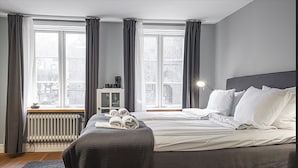 Een slaapkamer met een groot bed, een nachtkastje, een lamp en uitzicht op een stadsbeeld door het raam.