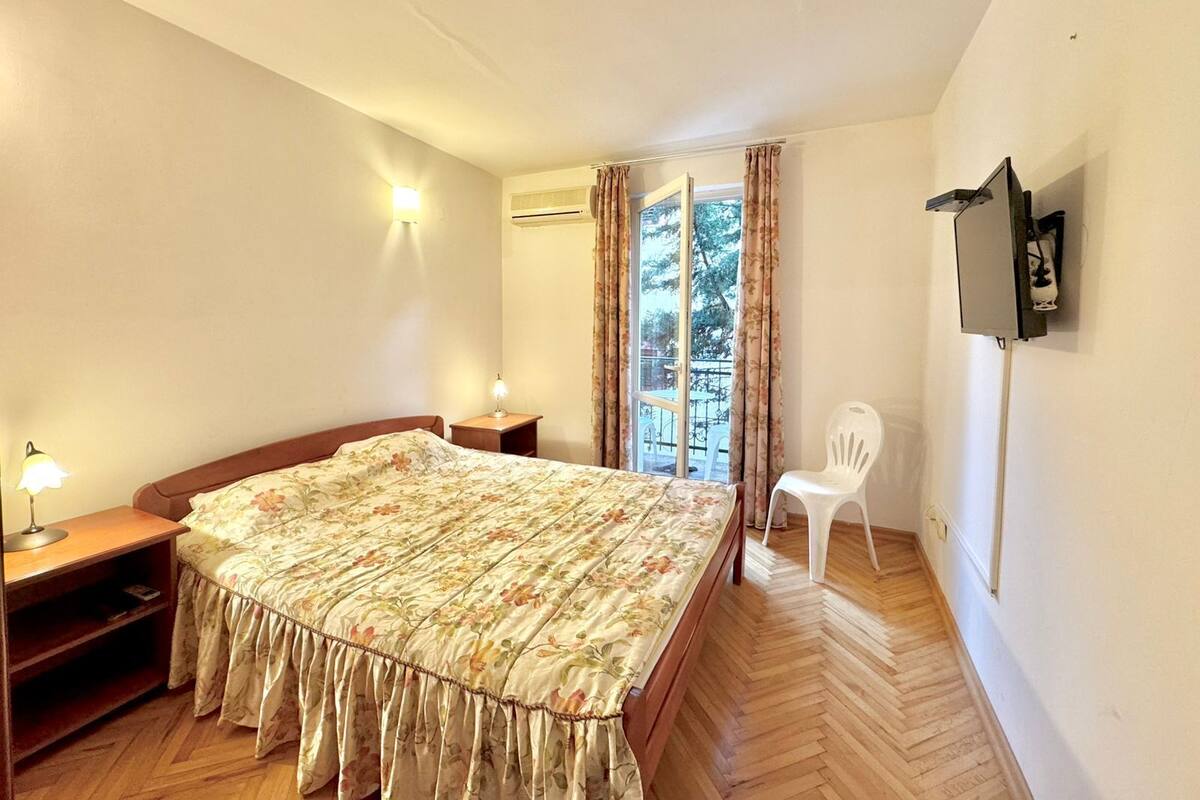 Ein Schlafzimmer mit einem hölzernen Bett, einem Nachttisch, einem Schreibtisch, einem Stuhl und einem an der Wand befestigten Fernseher.