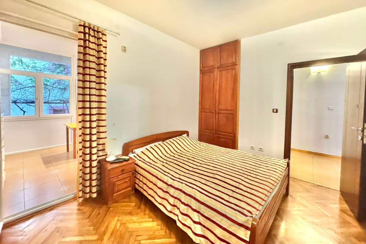 Ein Schlafzimmer mit einem hölzernen Bett, einem Nachttisch, einem Kleiderschrank und einer Glastür, die auf einen Balkon führt.