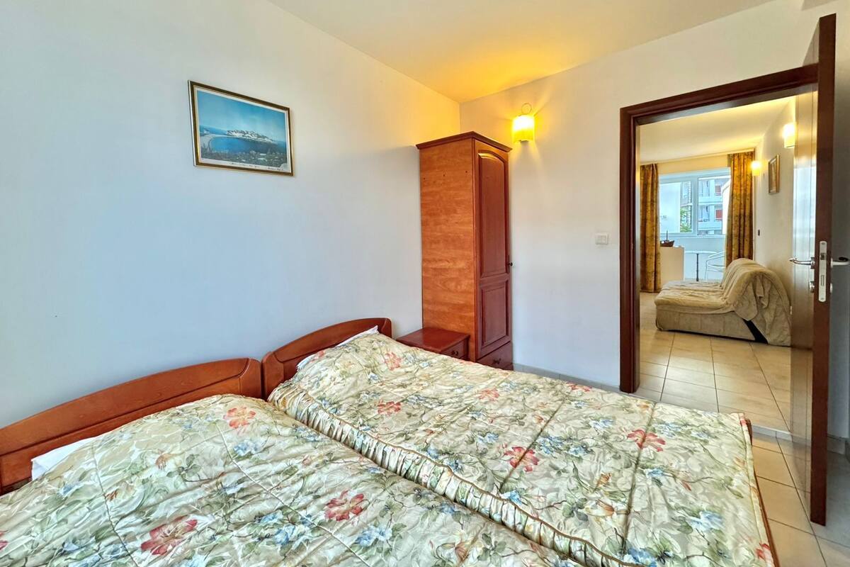 Ein Schlafzimmer mit einem Bett, einem Holzschrank, einer Wandleuchte und einem Fenster mit Vorhängen.