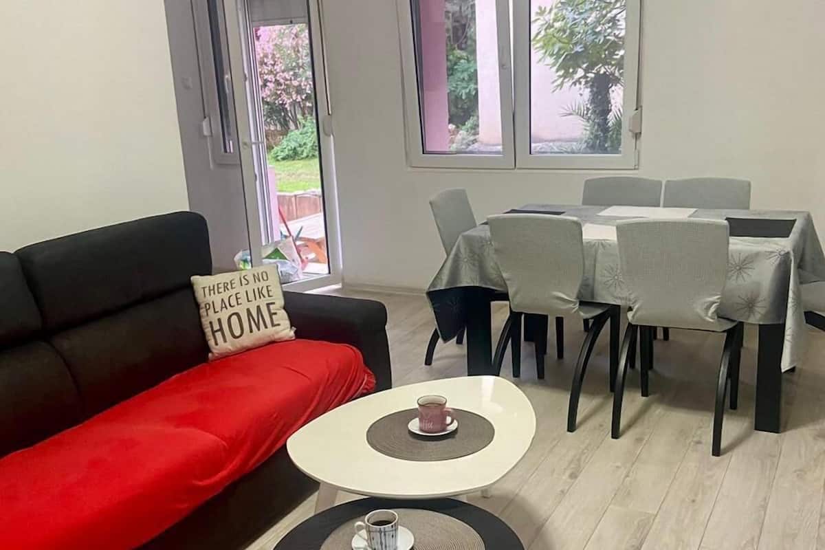 Ein Wohnzimmer mit einer schwarzen Couch, einem roten Kissen, einem Couchtisch und einem Essbereich mit Stühlen und einem Tisch.